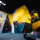 a group of people on a climbing wall in a room with a climbing wall in the background and a climbing wall in the foreground