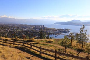 Panoramic view of Kelowna showcasing the cityscape, Okanagan Lake, and surrounding hills on a sunny day.