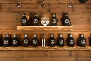 a wooden shelf filled with bottles and a whisk on top of a wooden wall next to a wooden wall, at Kelowna Beer Institute in Kelowna.