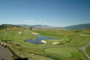 A view of a golf course with a pond in the middle of the course and mountains in the background at Predator Ridge Golf Resort in Vernon.