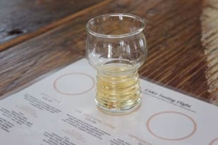 a glass filled with liquid sitting on top of a wooden table next to a paper with a list on it