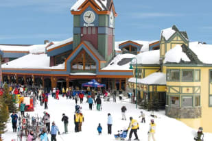 a crowd of people standing around a building with a clock on the top of its tower in the middle of a snow-covered area
