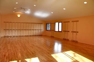 a large empty room with wooden floors and a fan in the corner of the room and a window on the far side of the room