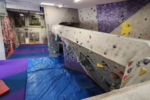 An indoor climbing gym with climbing walls, ropes, and equipment on the walls and floor.