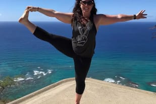 A woman standing on a ledge with her arms outstretched in the air with a view of the ocean in the background.