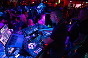 a dj mixing in front of a crowd of people at a party with laptops and sound equipment on the counter