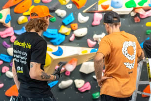 a couple of men standing next to each other near a wall covered in fake rocks and climbing gear and climbing equipment
