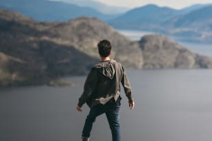 A person standing on a rock overlooking the scenic mountains and water in Peachland.