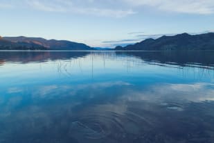 View of Osoyoos Lake with mountains in the background and reflections on the calm water.