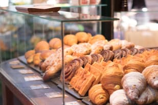 An assortment of pastries, including croissants, scones, and danishes, displayed inside a glass case at a bakery.