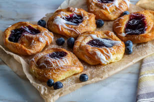 A tray of glazed berry Danish pastries with blueberries on parchment paper.