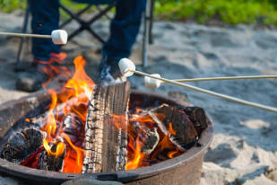Marshmallows being roasted on sticks over a blazing campfire, with