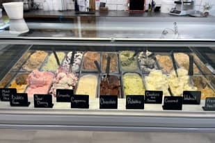 Various gelato flavors including Bubble Gum, Sour Cherry, Amaretto, Cappuccino, Chocolate, Pistachio, Cookies and Cream, Coconut, Walnut, and French Vanilla displayed in a counter at Gigi's Gourmet Gyros and Gelato in Summerland.
