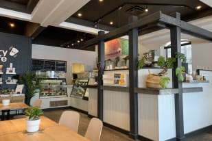 Interior of a cozy café named "beanery café" in Summerland, featuring wooden tables, potted plants, a menu board, and a counter with glass display cases.