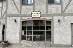 The exterior of a quaint cafe named "Country Café" with a Tudor-style design and a large window displaying statues. Summerland.