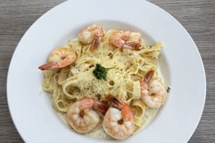 A plate of fettuccine pasta with creamy sauce and garnished with shrimp and parsley, served on a wooden table.