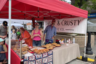 A bakery stall with a "Sweet & Crusty Bake Co." sign and various pastries on display at an outdoor market in Summerland.