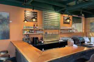 A cozy bar in Osoyoos with a wooden countertop, various drinks, a menu board showcasing different beers, and an assortment of glasses and beverages on shelves.