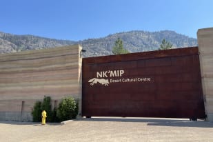 Entrance to the NK’MIP Desert Cultural Centre in Osoyoos with mountain backdrop under clear blue sky.