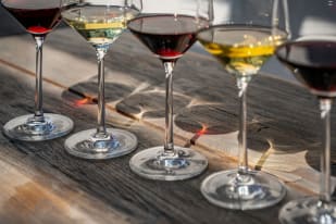 A close-up view of wine glasses filled with various colors of wine casting reflections on a wooden table in Vernon.