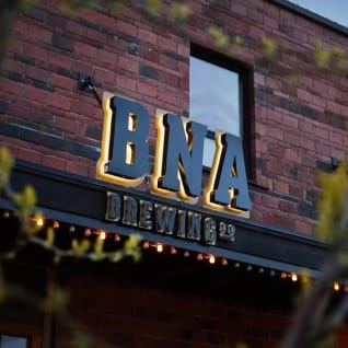 The exterior sign of BNA Brewing in Kelowna, featuring illuminated letters against a brick building.