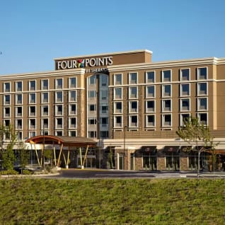 a large hotel with a plane flying over its roof and a grassy field in front of it.