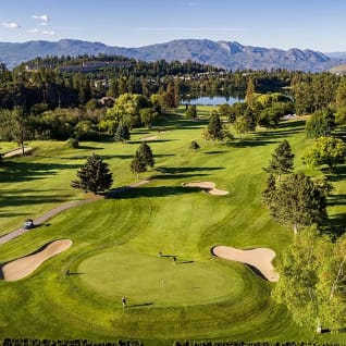 an aerial view of Shannon Lake Golf Course in West Kelowna with mountains in the background and a lake in the middle of the course