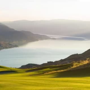 a view of a golf course with a lake and mountains in the background with a green and a golf ball in the foreground at The Rise Golf Course in Vernon