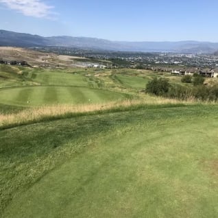 a view of a golf course from the top of a hill with a view of the city in the distance