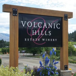 A sign reading Volcanic Hills Estate Winery with a backdrop of hills and vineyards in West Kelowna.