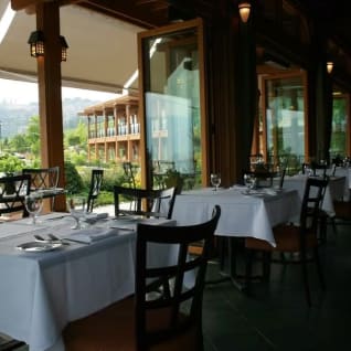 A scenic view of the dining area at Old Vines Restaurant at Quail's Gate Winery in Kelowna, with elegantly set tables and a backdrop of greenery and outdoor seating. Credit: Old Vines Restaurant at Quail's Gate Winery.