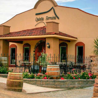 Quinta Ferreira Estate Winery building in Oliver, BC, featuring a Mediterranean-style facade with a tiled roof, outdoor seating, and rustic decor elements.