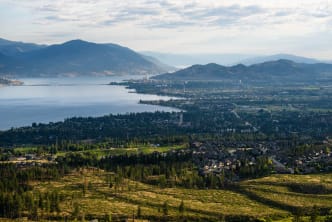 Aerial view of a city by a lake surrounded by mountains under a partly cloudy sky;