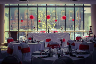 a banquet room set up for a wedding with red and white linens and pom pom balls hanging from the ceiling