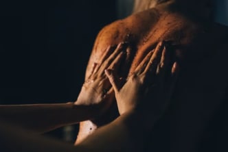 A woman with her hands on her chest and her hands covering her face with her hands in a dark room.