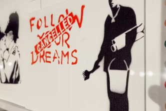 A picture of a man on a wall with the text Follow Your Dreams and the word Cancelled stamped over it.