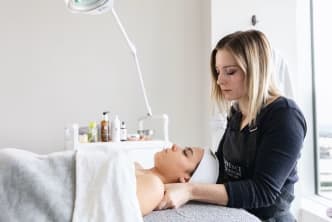 a woman getting a facial massage in a room with a large window and a white towel on the back of her head.