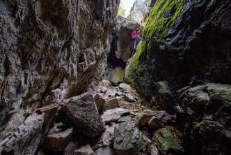 Climber ascending a moss-covered rock face in a narrow rocky canyon in Penticton.