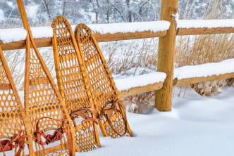 Vintage wooden snowshoes leaning against a wooden fence covered in snow in a winter landscape.