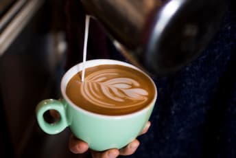 a person holding a cup of coffee in their hand with a latte on the side of the cup