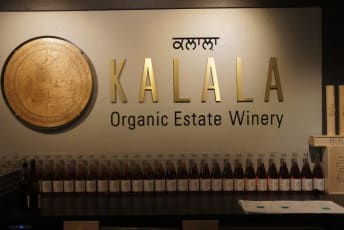 a sign that says kalala organic estate winery on the side of a wall with bottles of wine in front of it