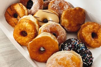 a box filled with lots of doughnuts on top of a wooden table next to a cup of coffee