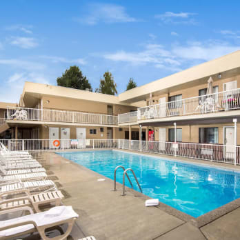 A motel courtyard with a swimming pool surrounded by white deck chairs under a clear blue sky.