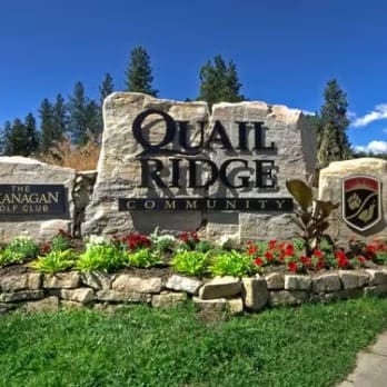 a sign for the quail ridge community in the middle of a grassy area with flowers in the foreground and trees in the background.