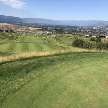 a view of a golf course from the top of a hill with a view of the city in the distance