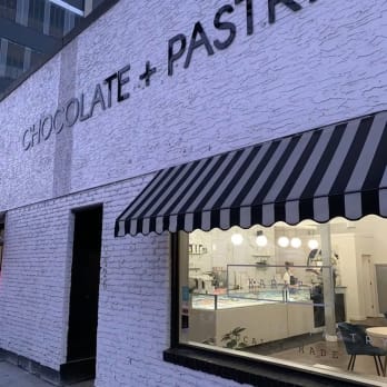 A white brick building with a black and white awning on the front and a black and white striped awning on the side displaying CHOCOLATE + PASTRY, identified as Karat Chocolate & Pastry Boutique in Kelowna.