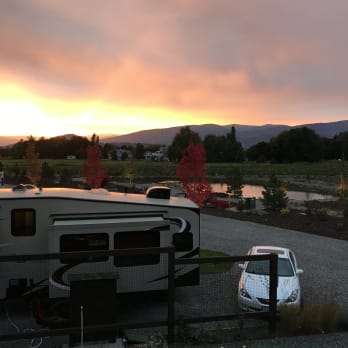 Sunset view at Kelowna Urban Farm and RV Park, with RVs and cars parked in the foreground and mountains in the background.