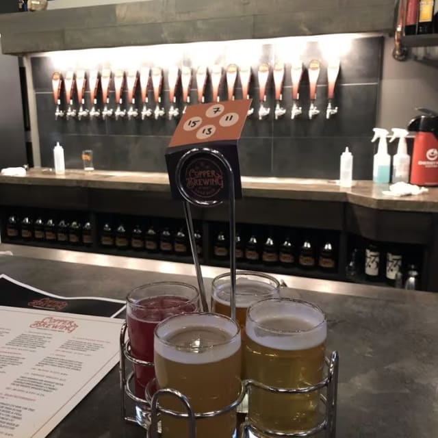 Three glasses of beer sitting on a table in front of a menu and a drink dispenser at Copper Brewing Co. in Kelowna.