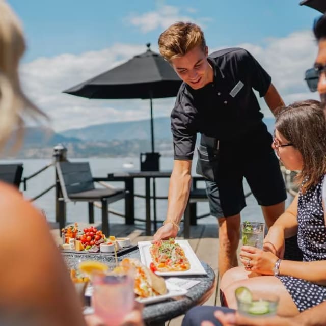 A group of people sitting around a table with food and drinks, overlooking the ocean at Hotel Eldorado in Kelowna.