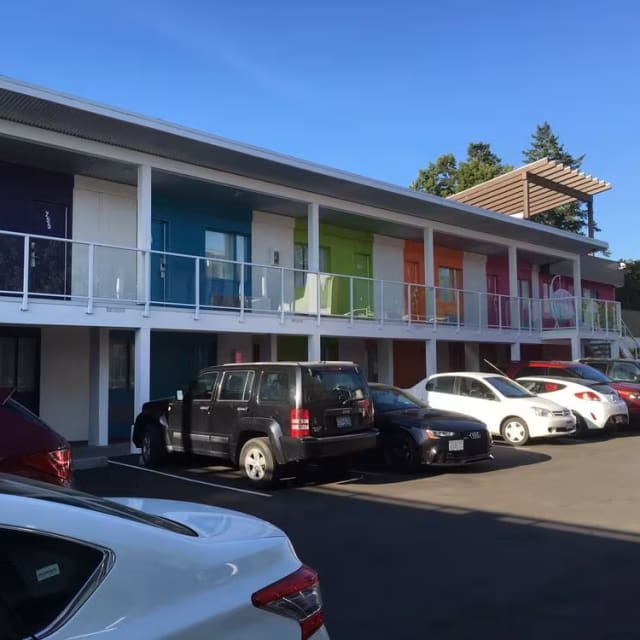 a row of parked cars in front of a multi-story building with balconies and colorful doorways.